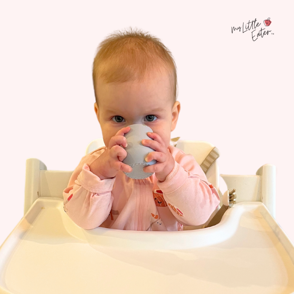 Baby using two hands to easily lift the EZPZ tiny cup to drink water.