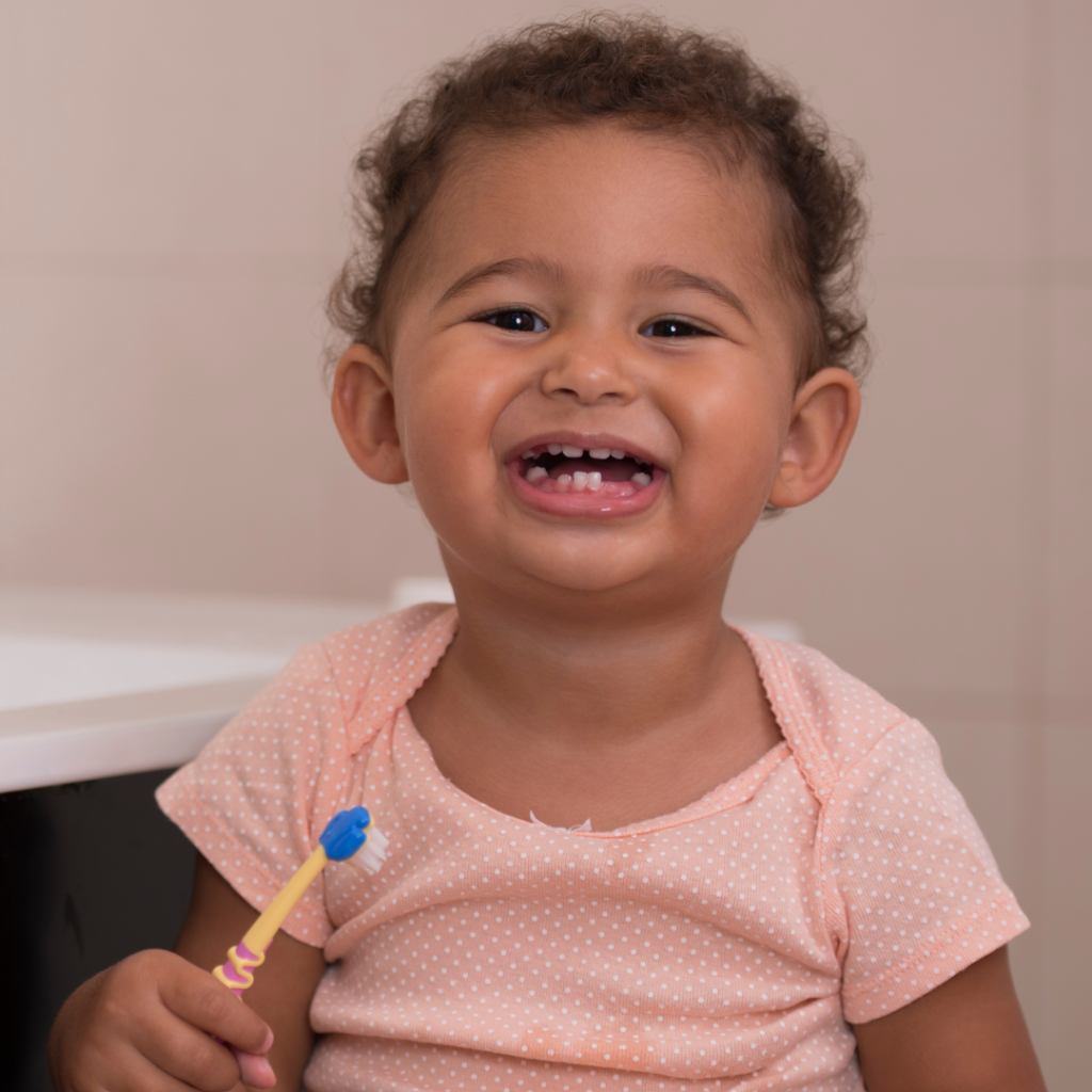 Smiling toddler holding a toothbrush for brushing their baby teeth.