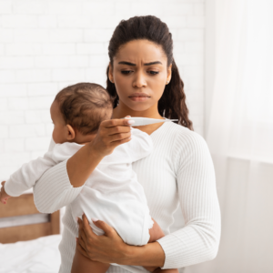 A mother holds their baby while looking at their temperature on a thermometer.