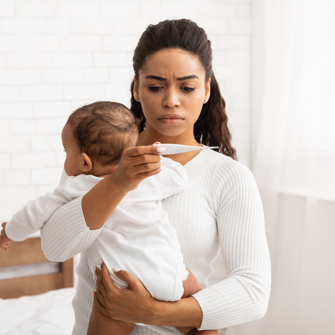 A mother holds their baby while looking at their temperature on a thermometer.
