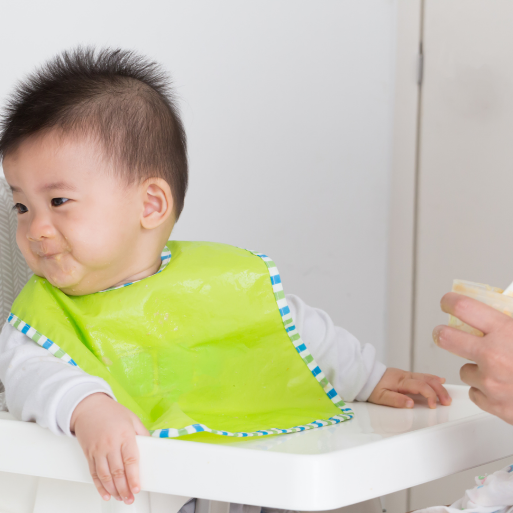 Baby refuses to eat solids while sitting in their highchair wearing a bib.