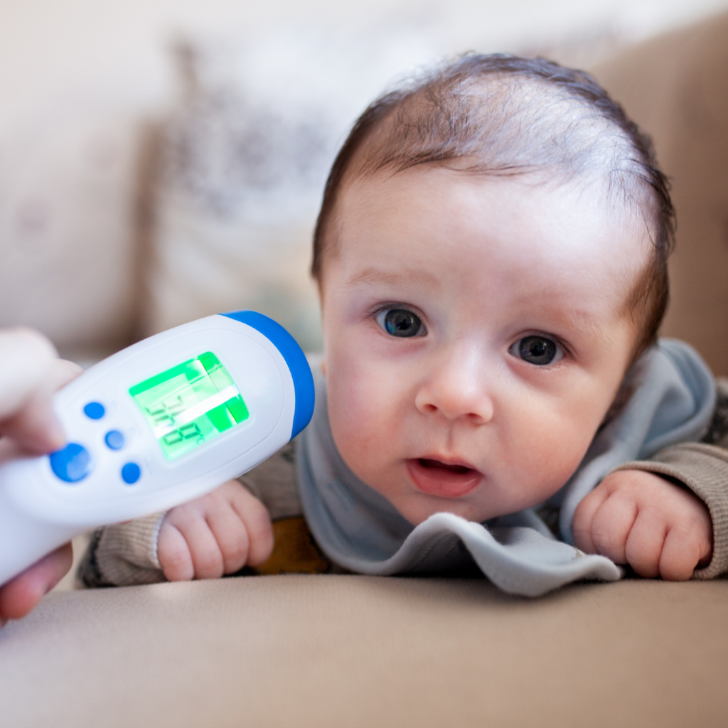 A baby is laying on their tummy on a couch while they get checked for a fever.