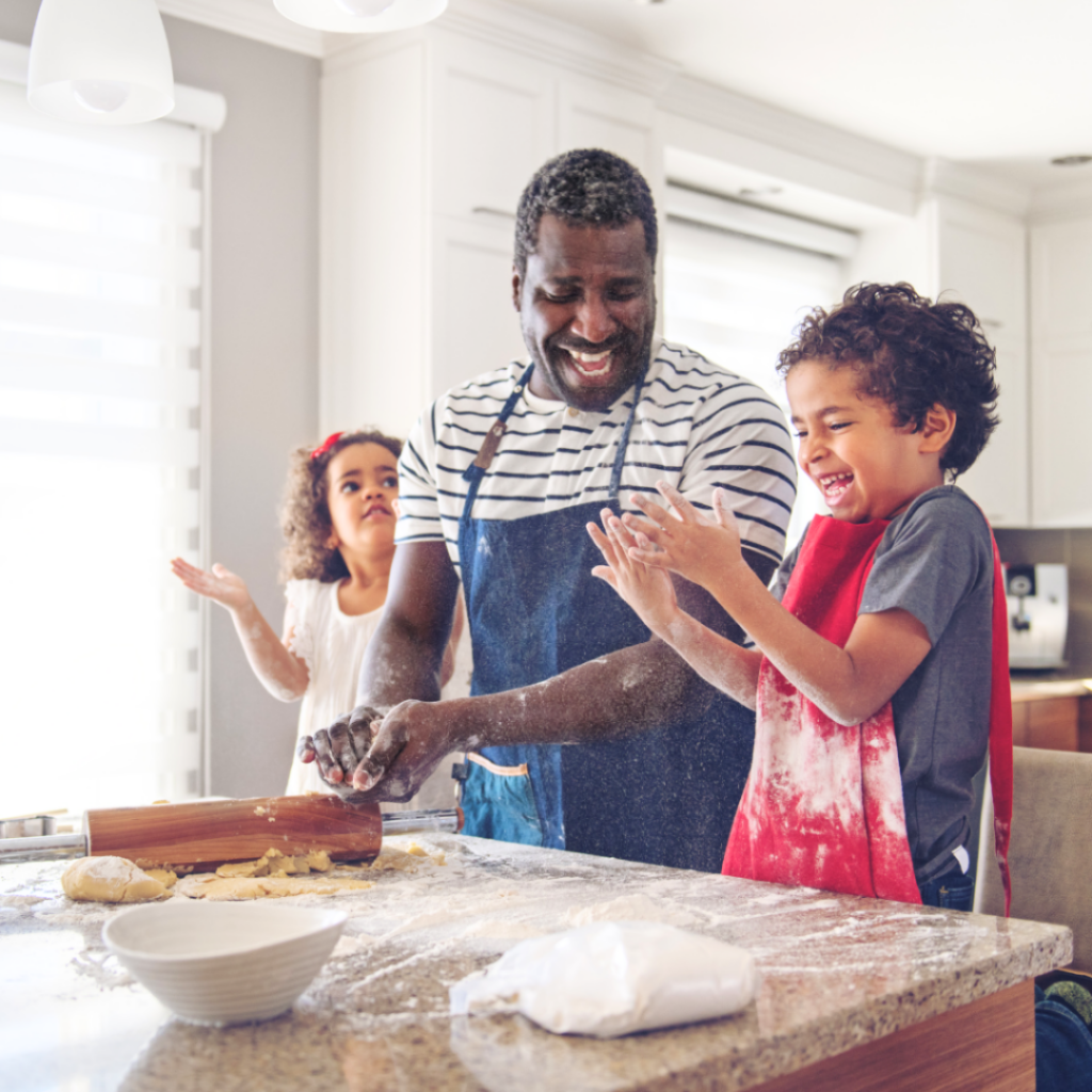 A dad and two little ones enjoying cooking together, laughing while they make dough.