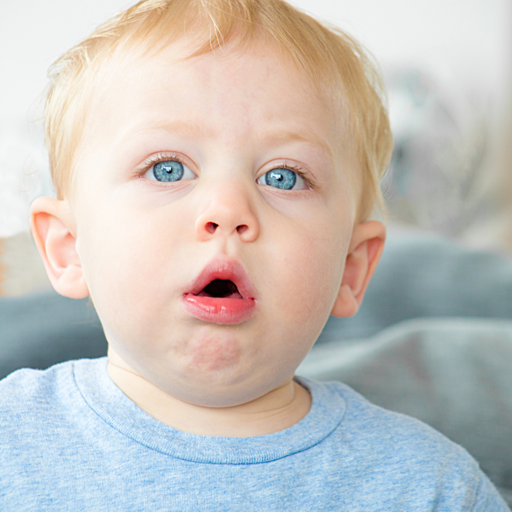 Baby that has started to eat solid food is gagging and coughing up something with eyes wide.