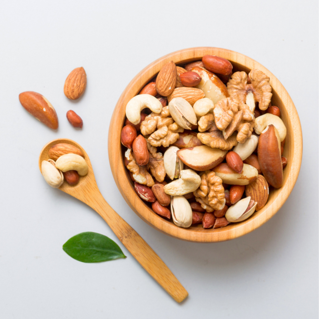 A bowl filled with various whole nuts including walnuts, cashews, almonds, and other nuts with a spoon beside it.