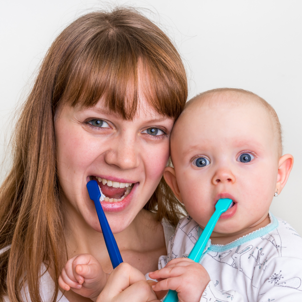 Both a parent and a baby brush their teeth together while the parent holds the baby.