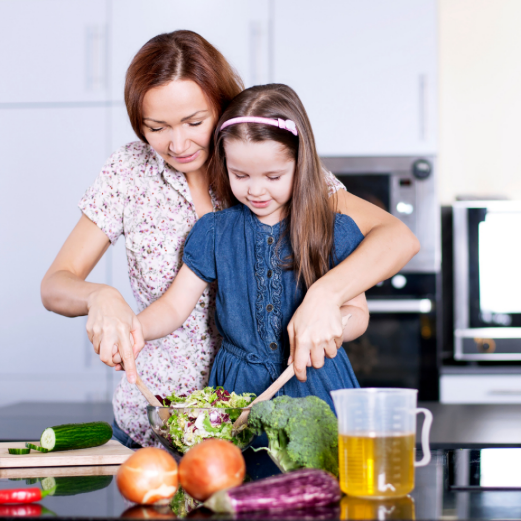 A child helps mix a salad with their parent.