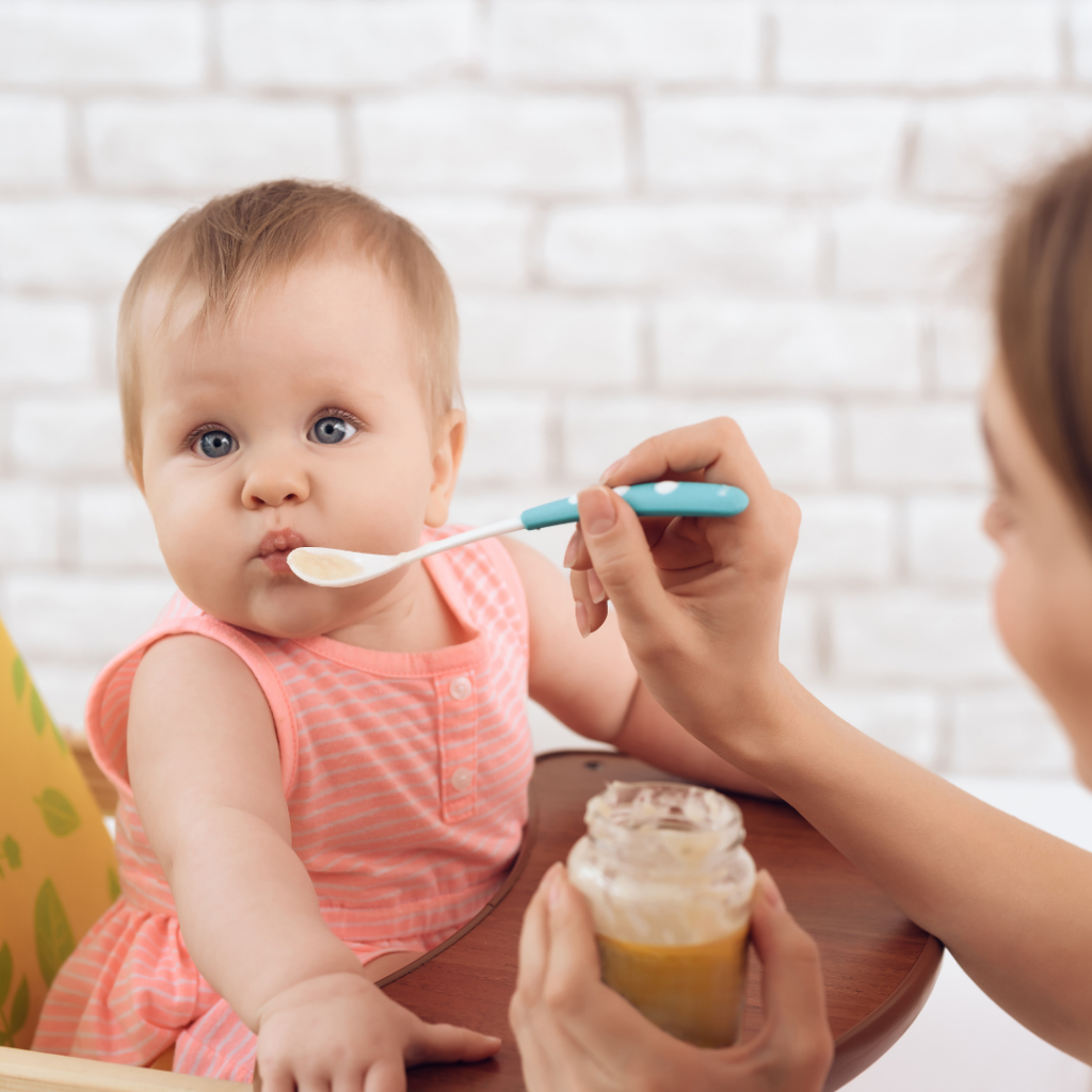 Baby being spoon fed a puree mixture while in their high chair.