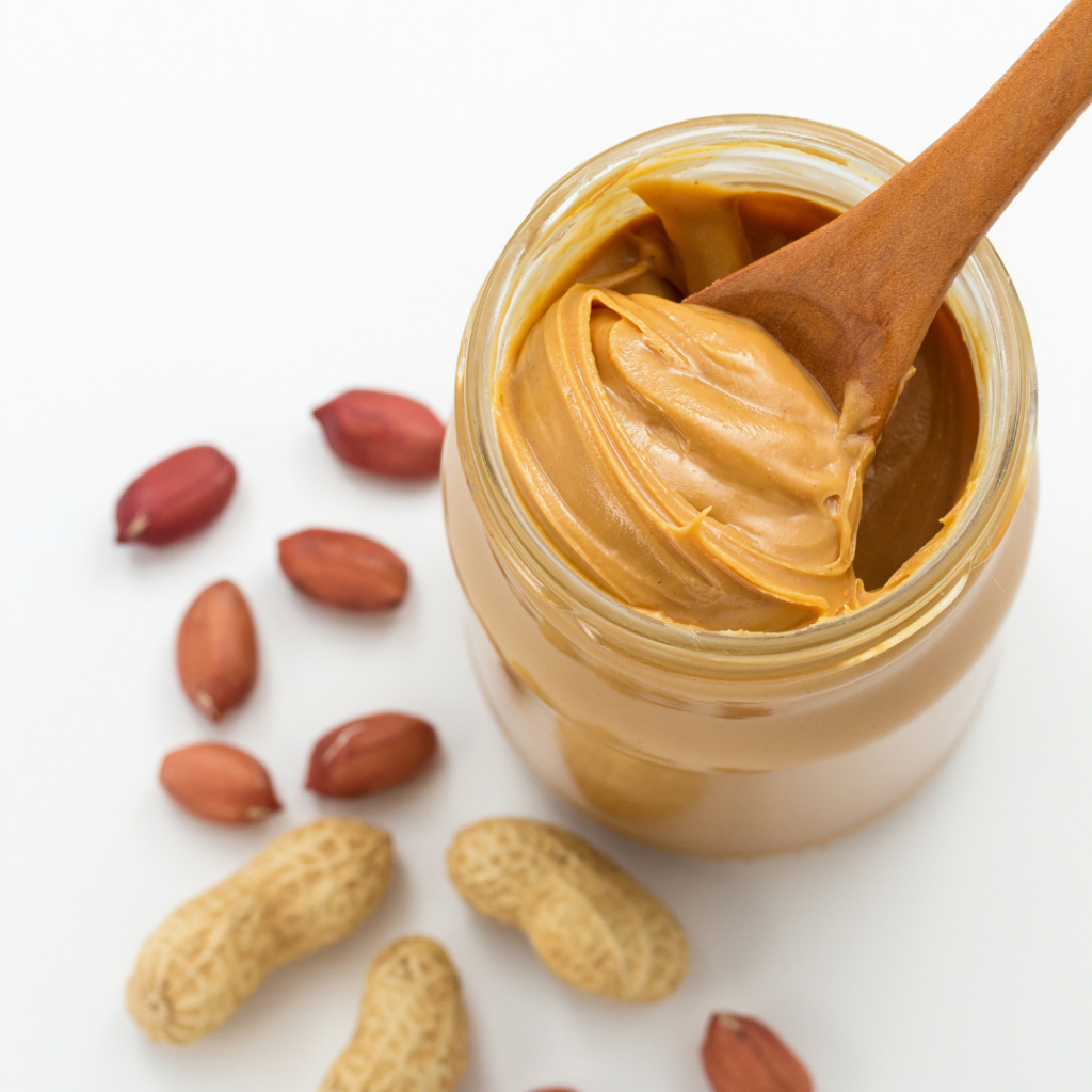 An open jar of peanut butter with whole peanuts surrounding the jar.