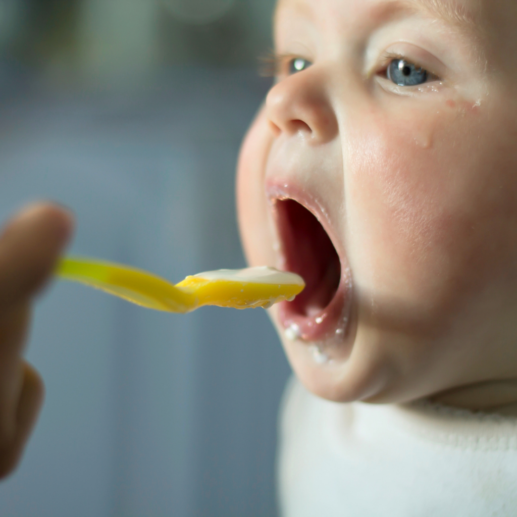 Baby with their mouth open for a spoonful of baby food to practice chewing skills.