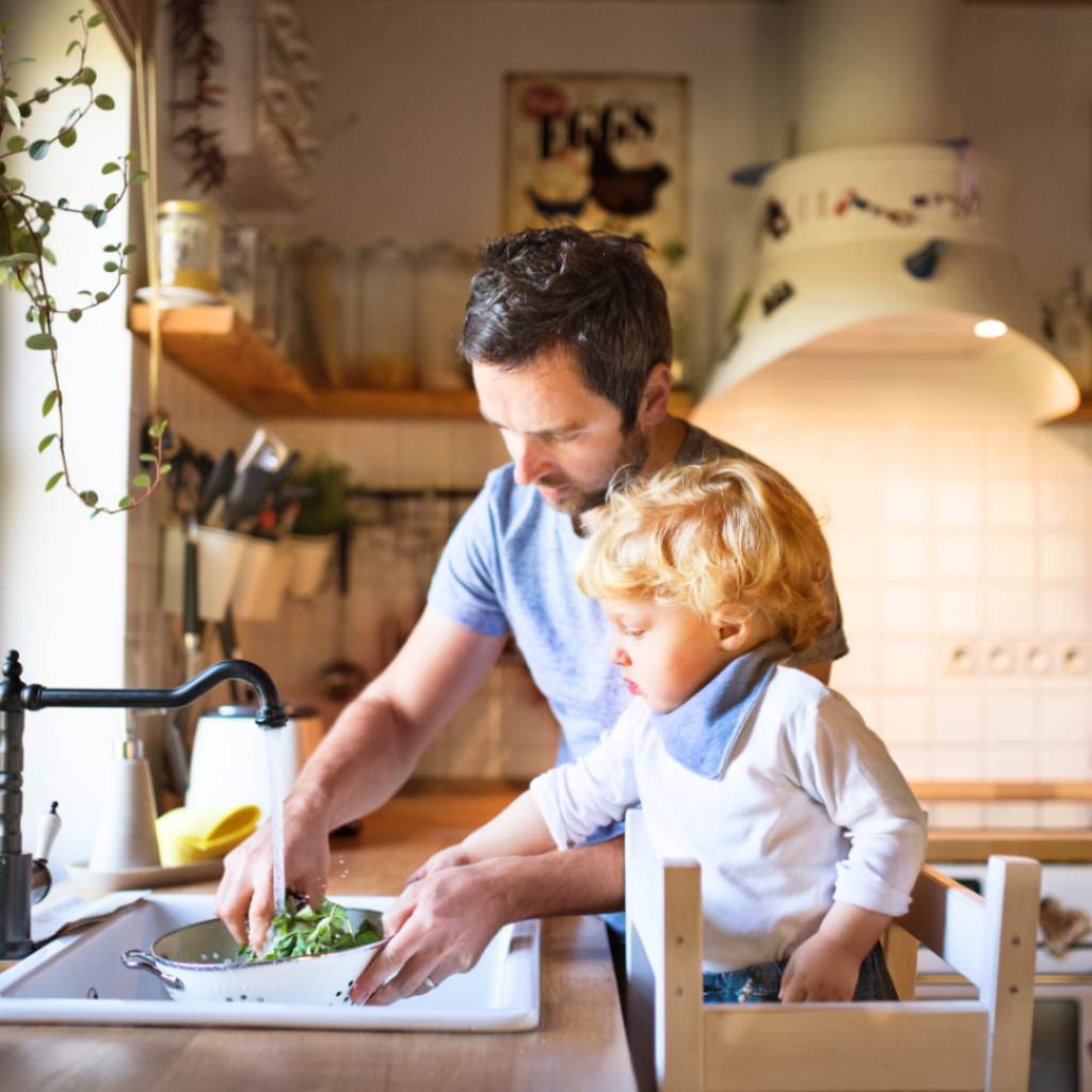 Toddler helps parent with washing lettuce at the sink in preparation for making easy recipes with them.