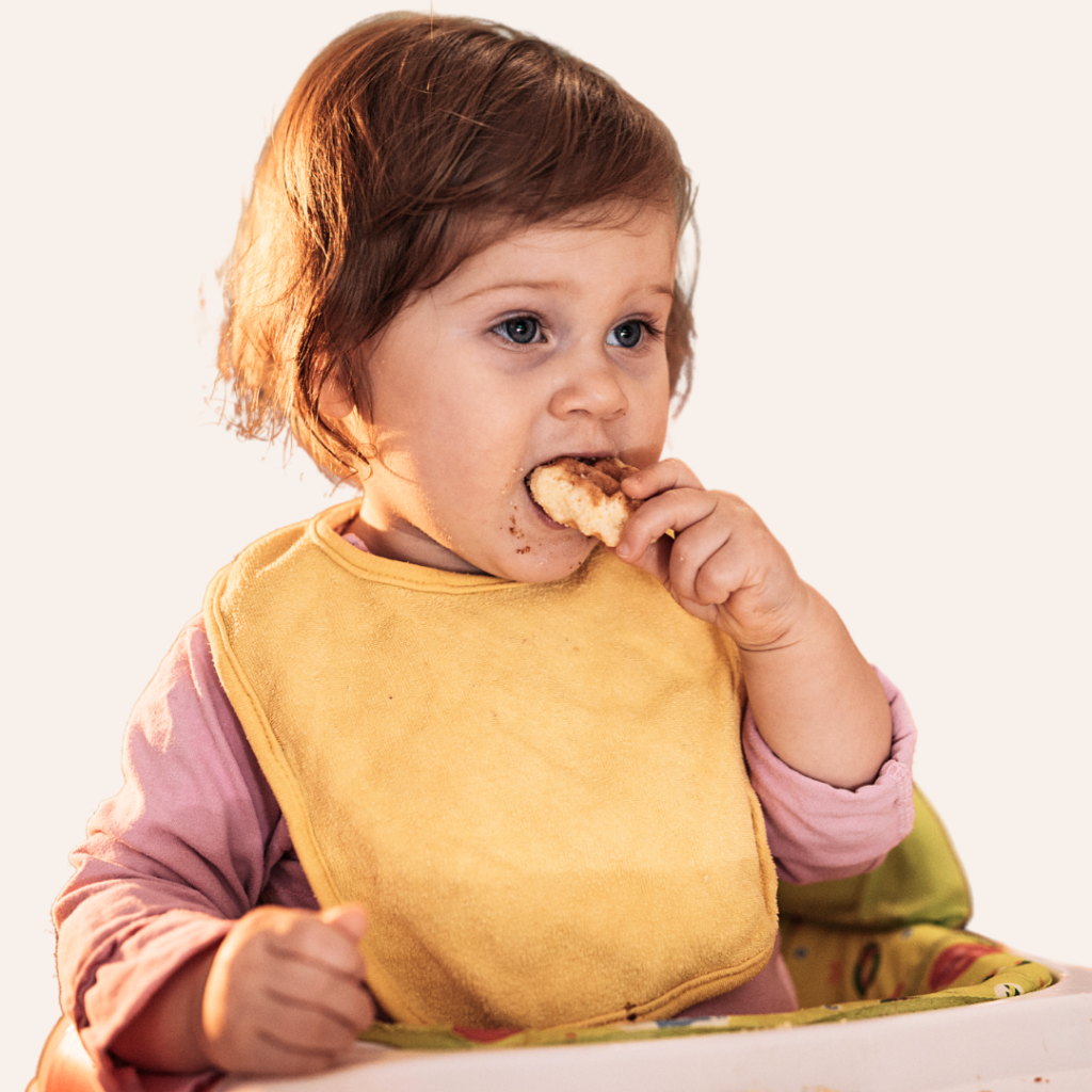 Toddler taking bites and chewing food while in their high chair.