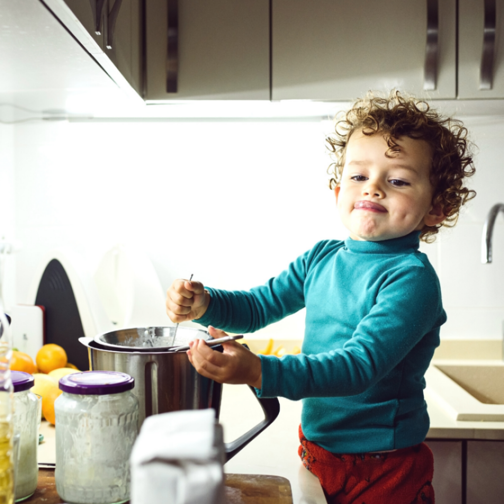 Toddler stands at the counter measuring ingredients and mixing them in a bowl, most toddlers love this task.