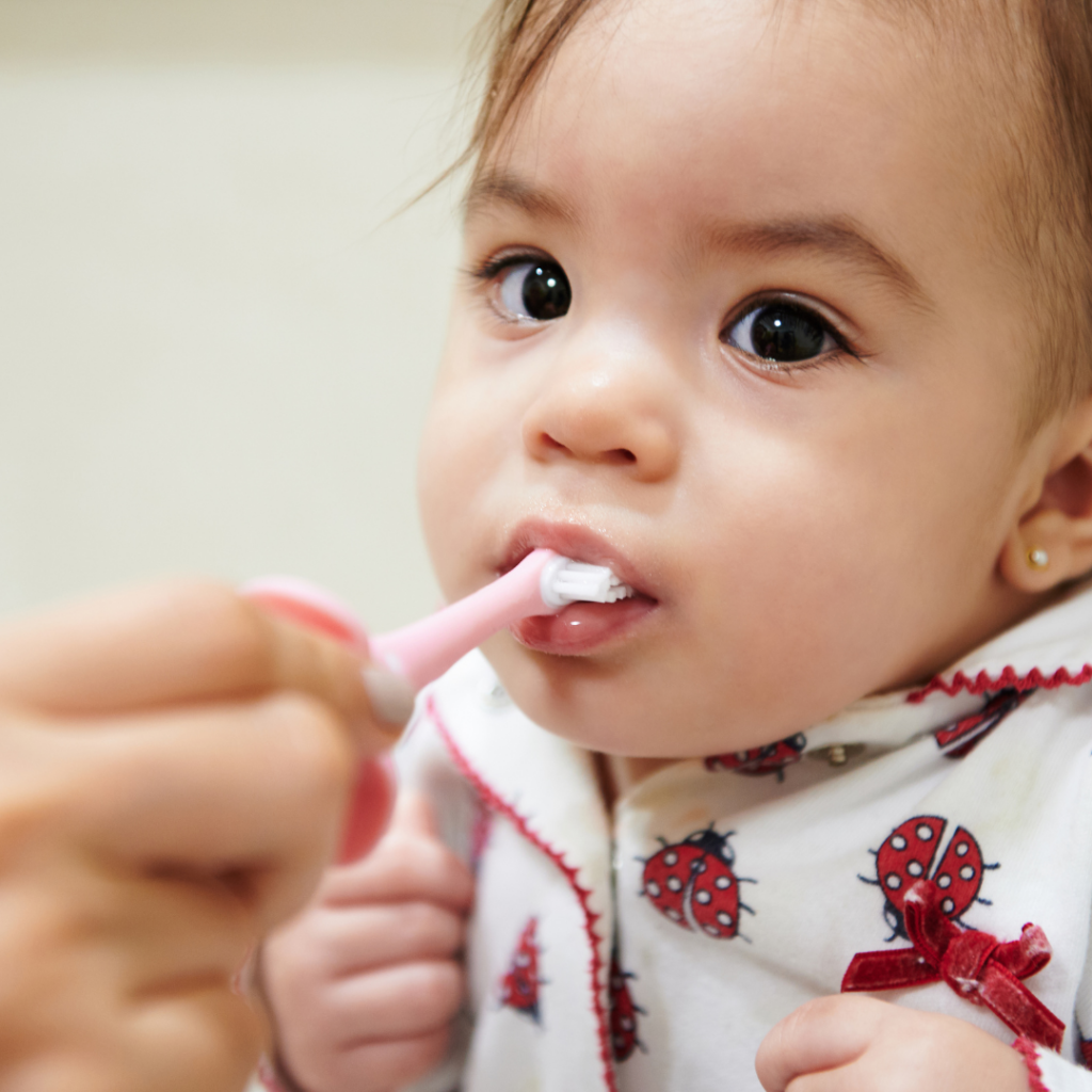 A baby is having their teeth brushed by their parent.