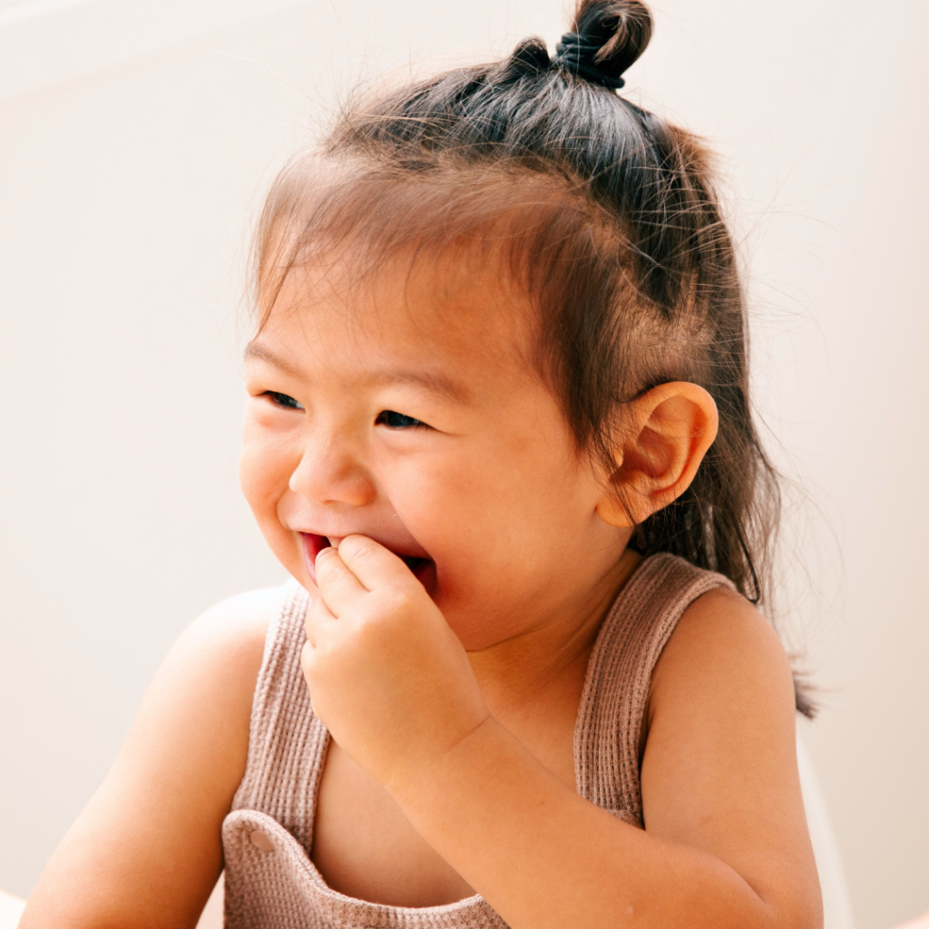 A baby smiles while bringing solid foods to their mouth.