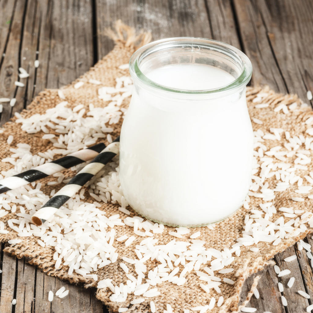 Rice milk in a glass jar with pieces of rice scattered around it.