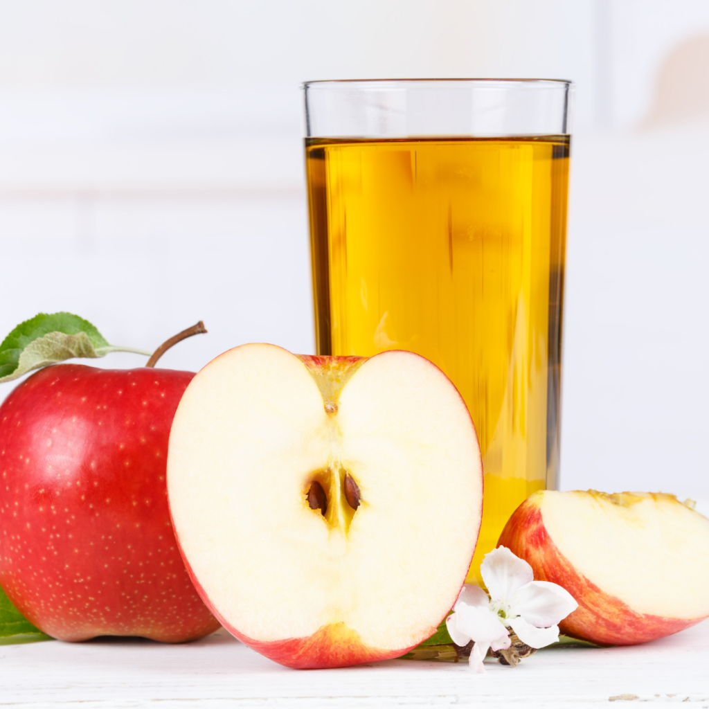 A glass of apple juice, high in toxic heavy metals, and fresh apples whole and cut beside it.