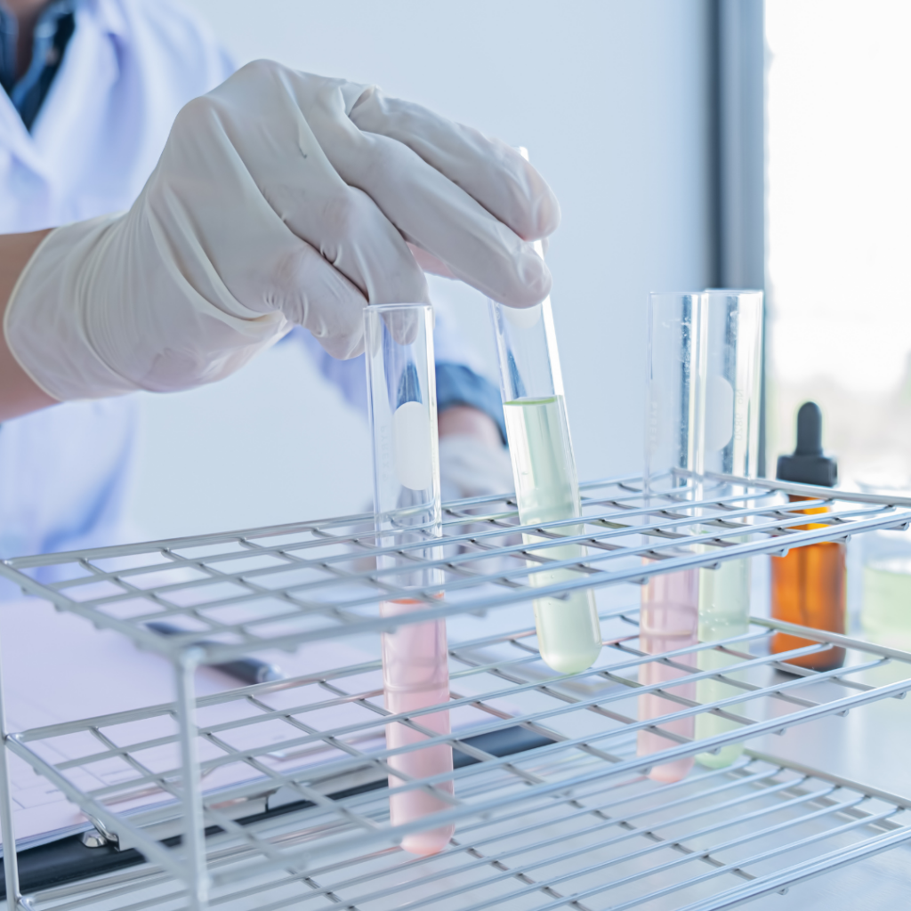 A scientist placing a test tube with colored liquid inside it into a test tube rack.