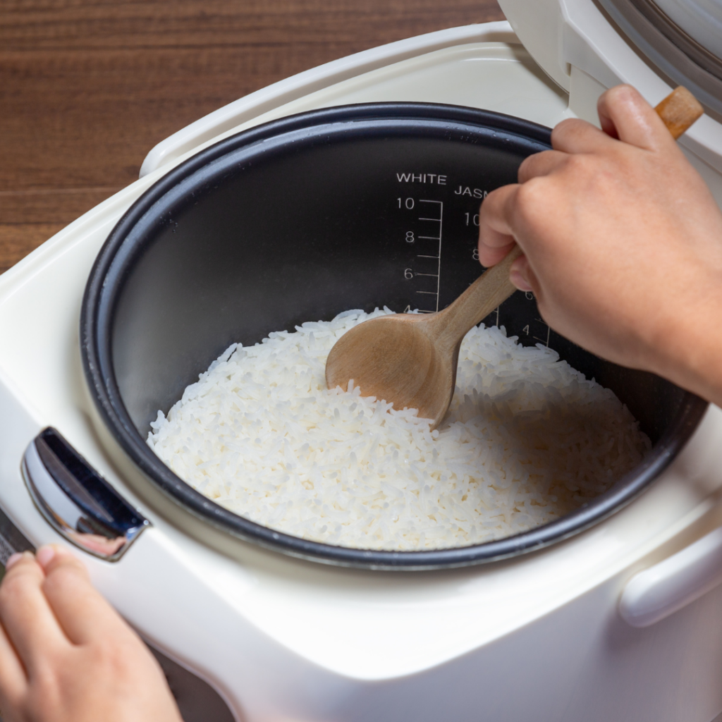 Rice in a rice cooker being stirred with a wooden spoon.