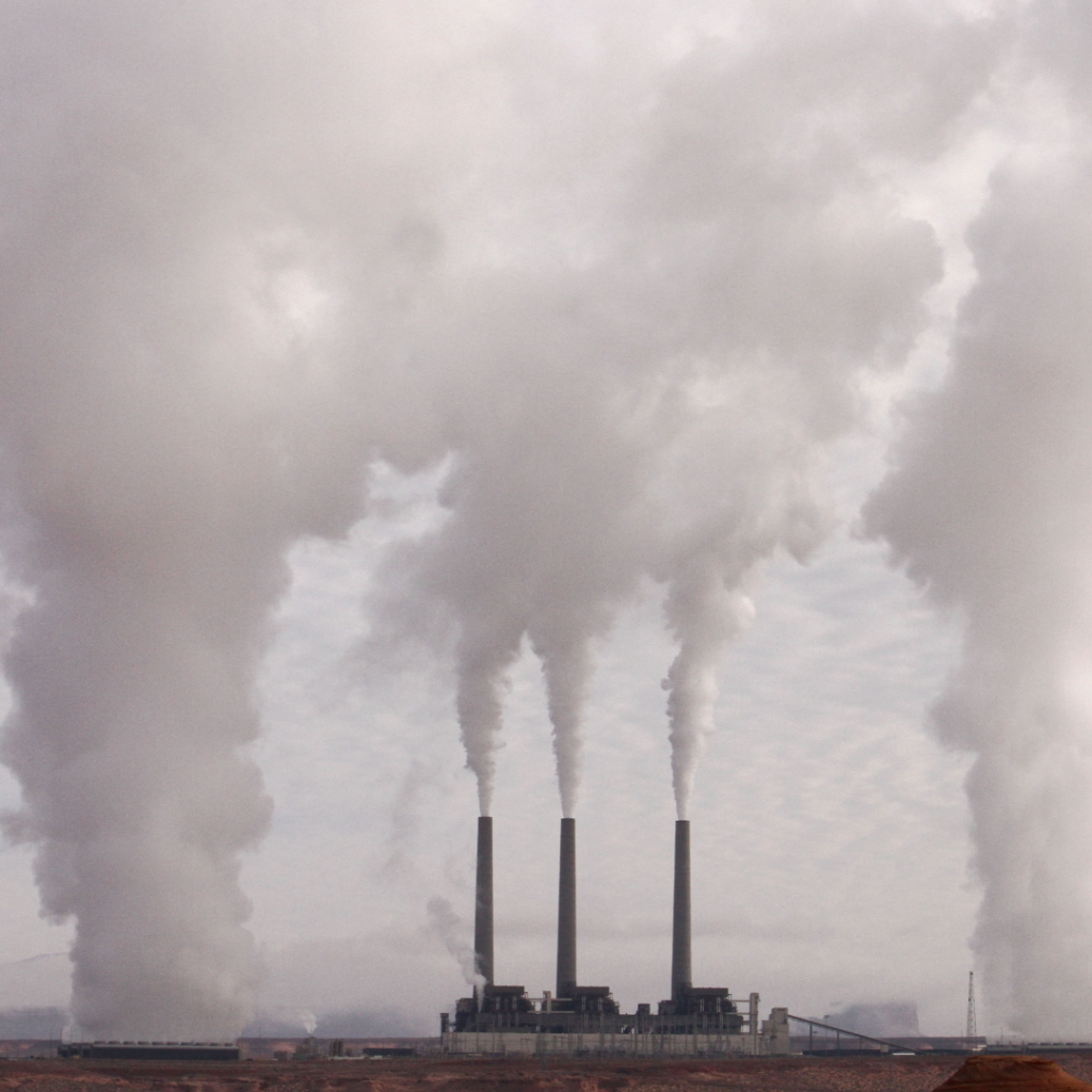 A factory shown in the distance with plumes of smoke filling the sky.