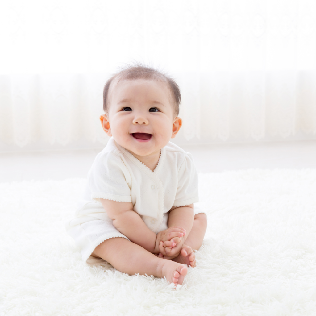 A baby smiles while sitting upright on the carpeted floor.