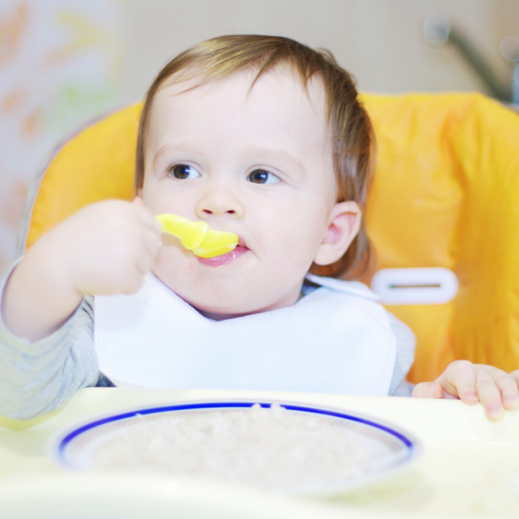 A baby in a high chair eating a spoonful of oatmeal.