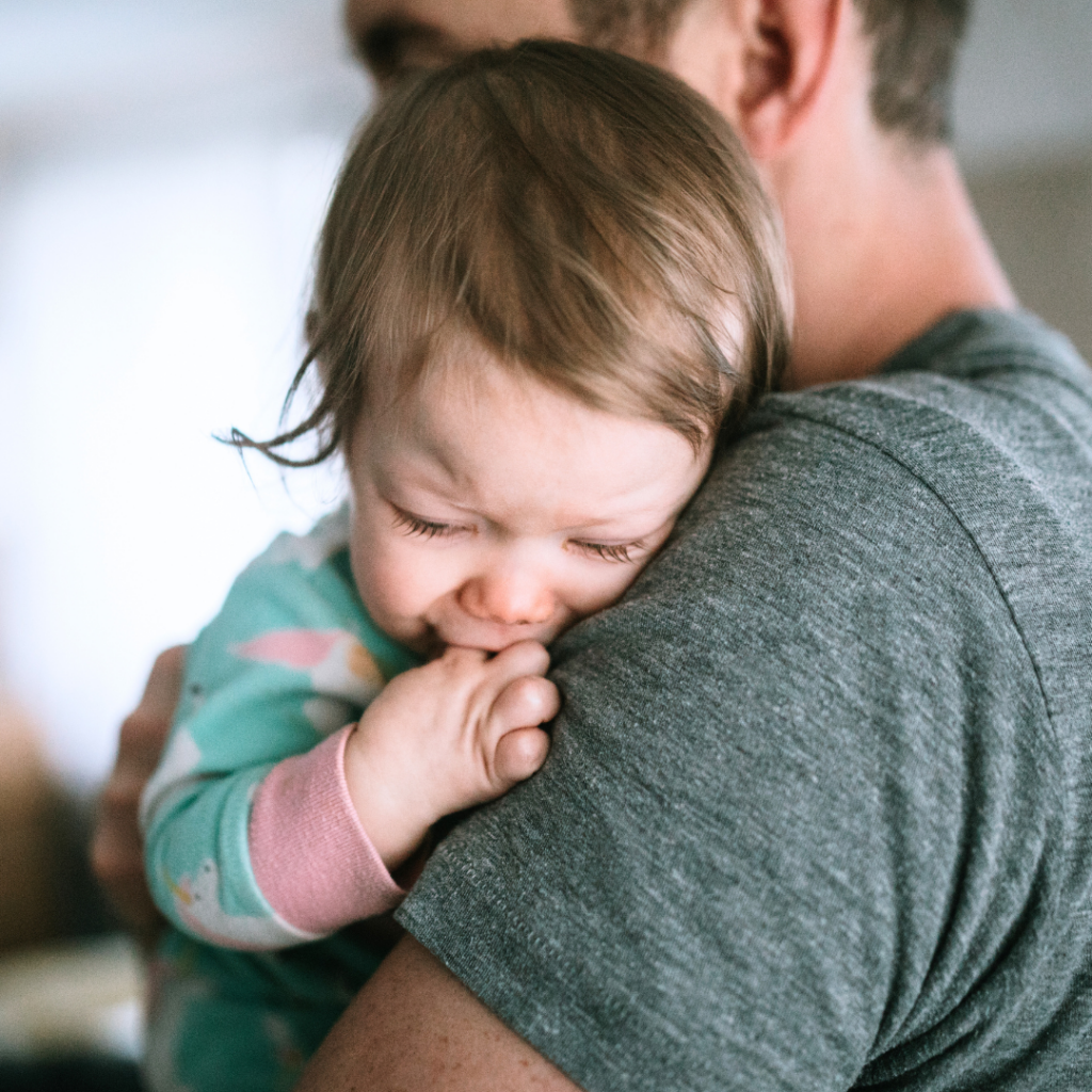 A baby cuddles in their parent's arms while they cry.