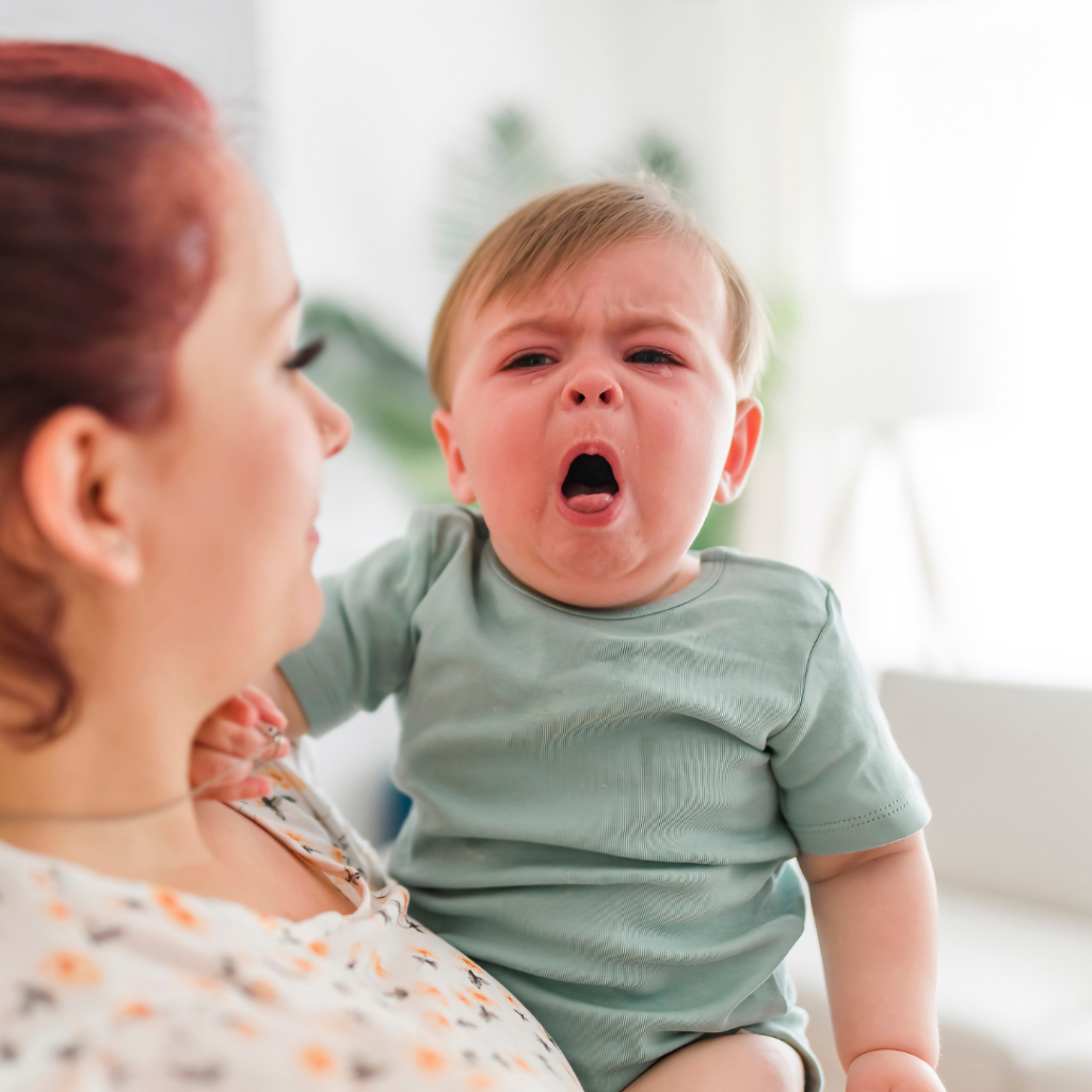 A mother holding her baby who has a red face and is crying and coughing.