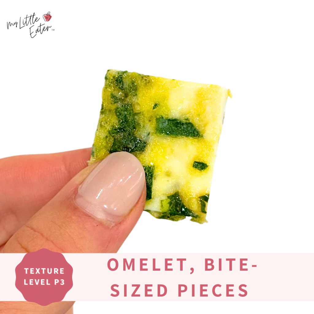 A baby egg omelet with spinach cut into bite-sized pieces being held in a pincer grasp.