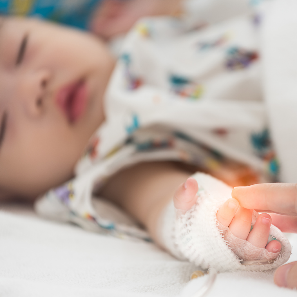 A baby in a hospital bed with an adult grasping their finger.