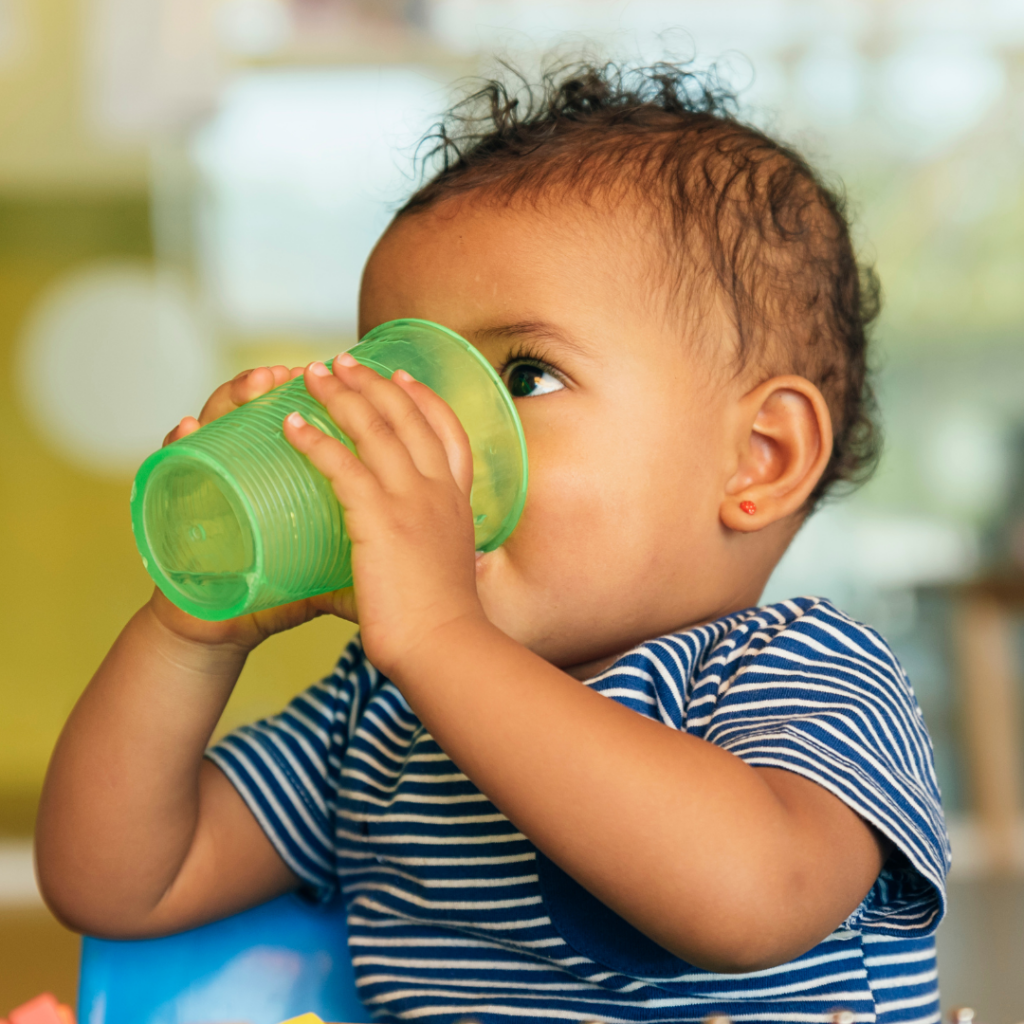 A baby holding an open cup and to drink water from it.