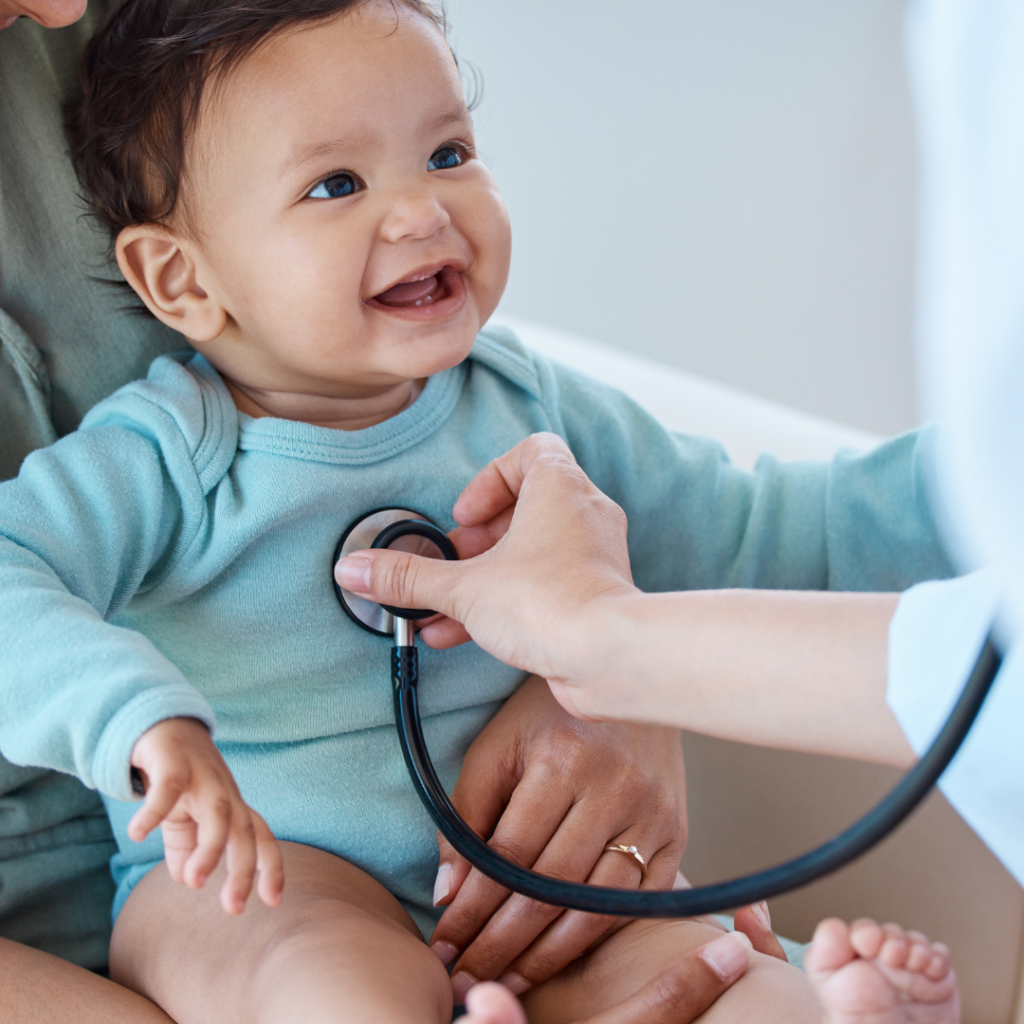 A baby smiling while being held and examined by a doctor.