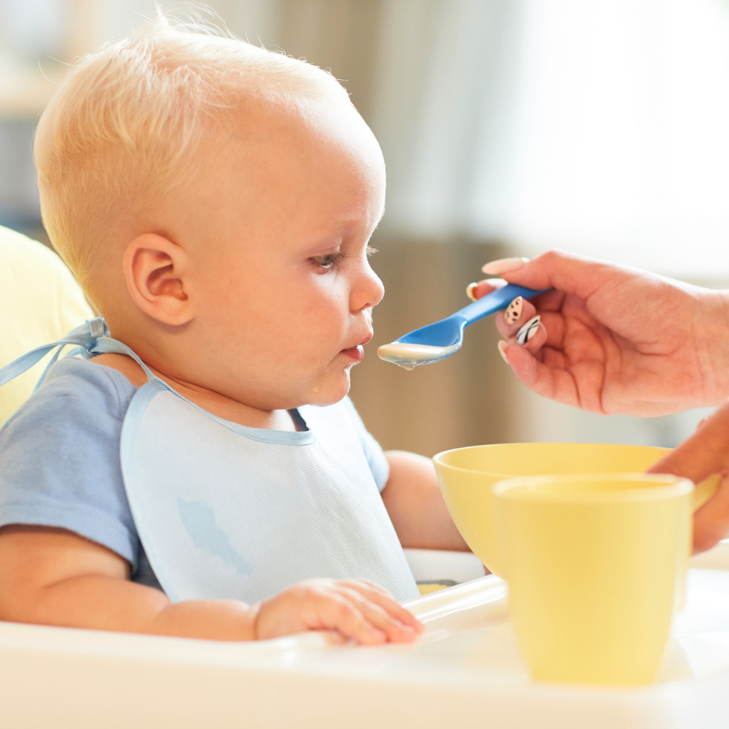 Baby being spoon-fed a puree with a cup of breast milk or water.