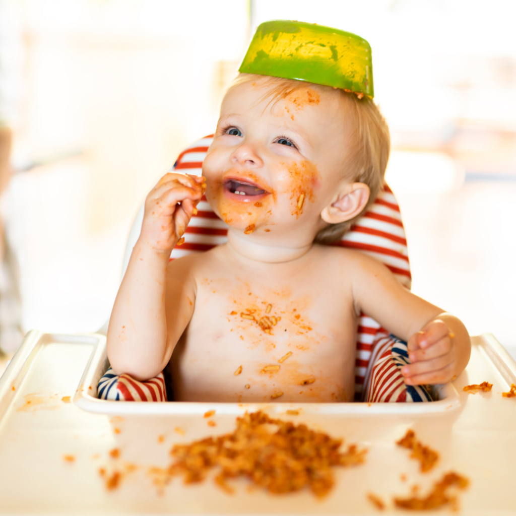 A baby in a highchair playing with their meal and making a mess.