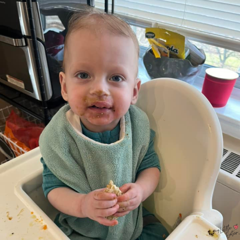 A toddler in their high chair with a mild allergic reaction on their cheeks from giving the baby eggs.