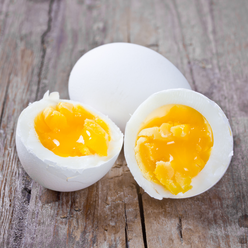 Split open boiled egg on a table with one cut in half showing slightly undercooked, runny yolks when babies need hard boiled eggs for safety.