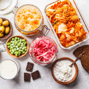 Overhead view of various fermented foods including kimchi, a glass of kefir, sauerkraut, olives, bread, peas, and more.