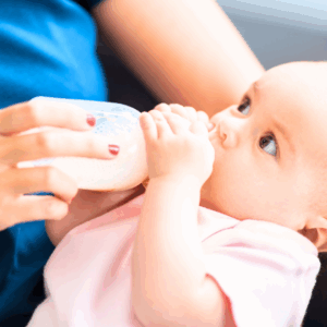 A baby drinking a goat-milk-based infant formula from a bottle while being held in her mother's arms.