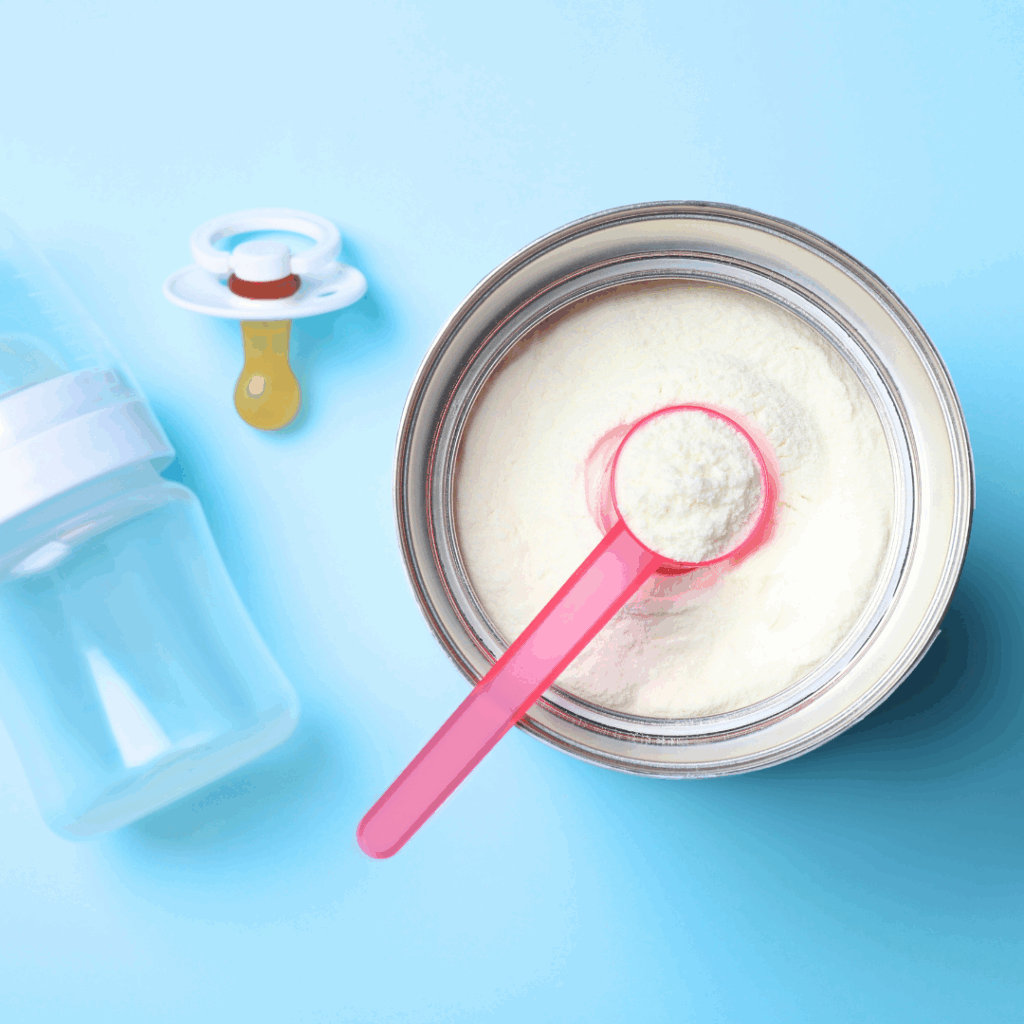 A container of Kabrita goat milk-based formula sits open with a scoop of formula powder inside, and a bottle beside it is ready to be filled with formula.