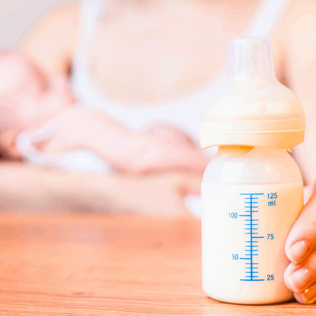 A mother holds a bottle of goat milk-based infant formula and is ready to feed her baby that she holds in her arms.