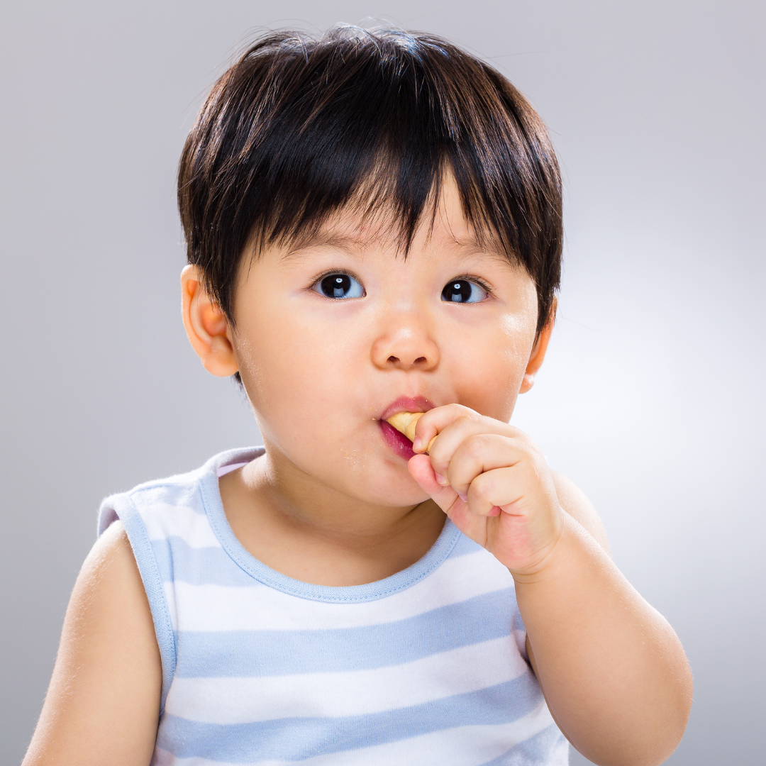 A baby boy eats a finger food using his palmar grasp