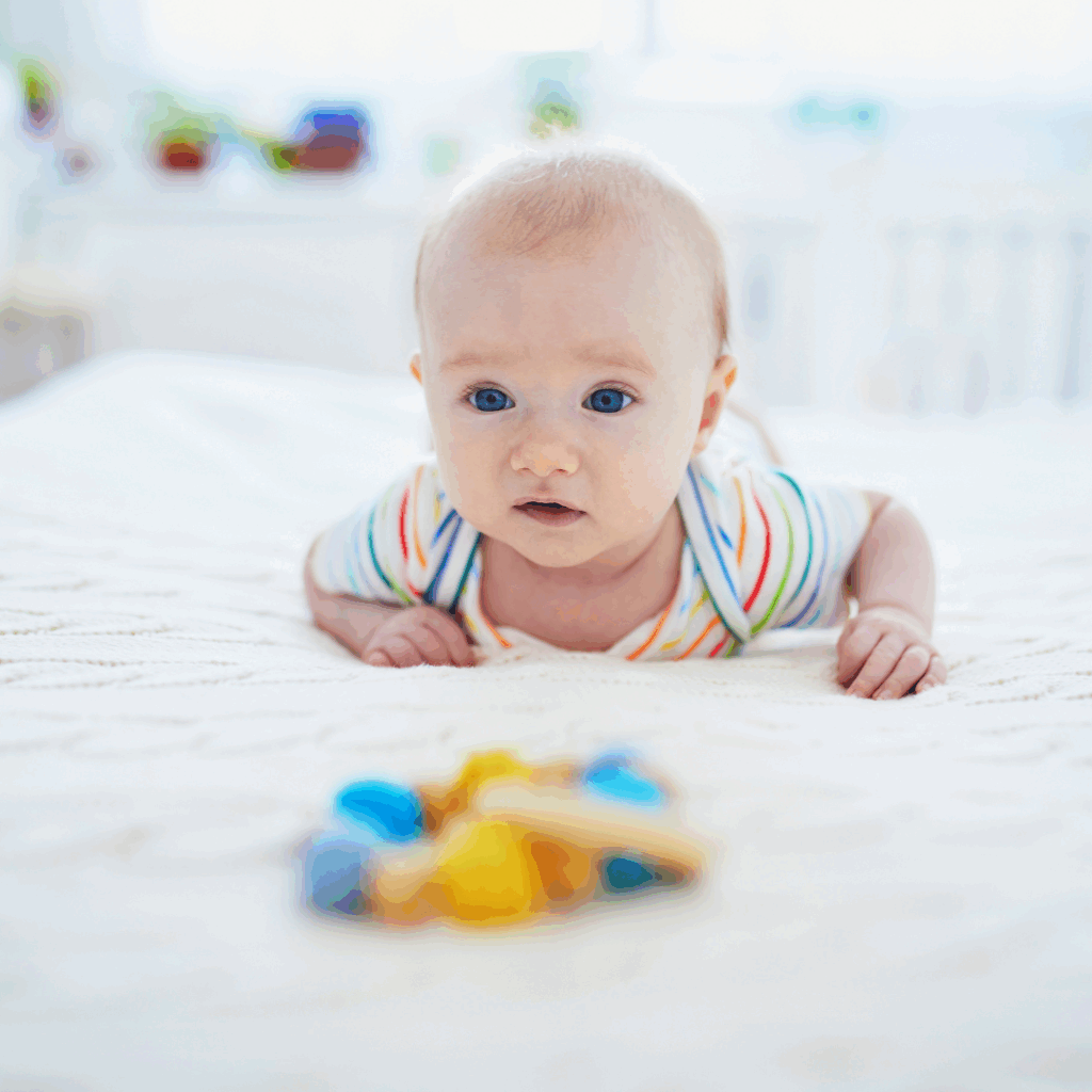 A baby lies on their tummy for tummy time, a toy in front of them.