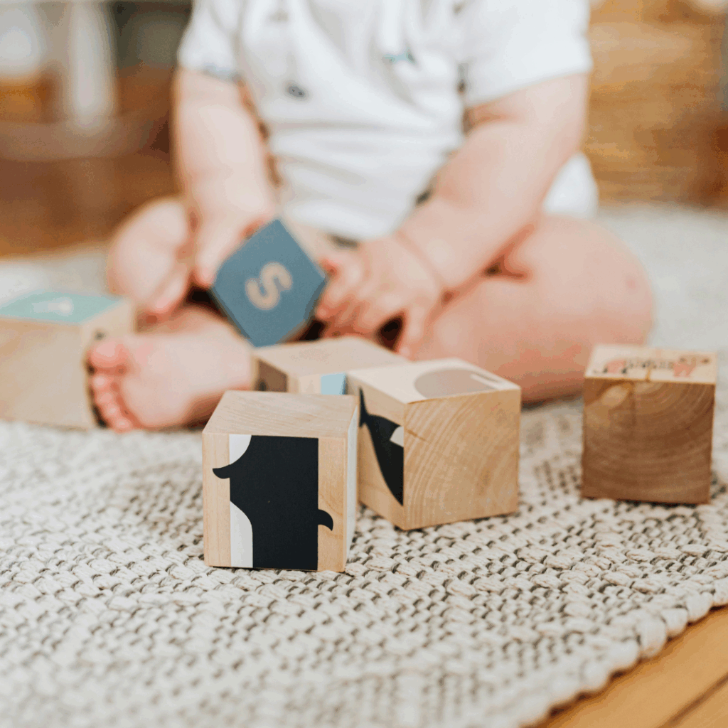 A baby sits on the ground and plays with wooden blocks.