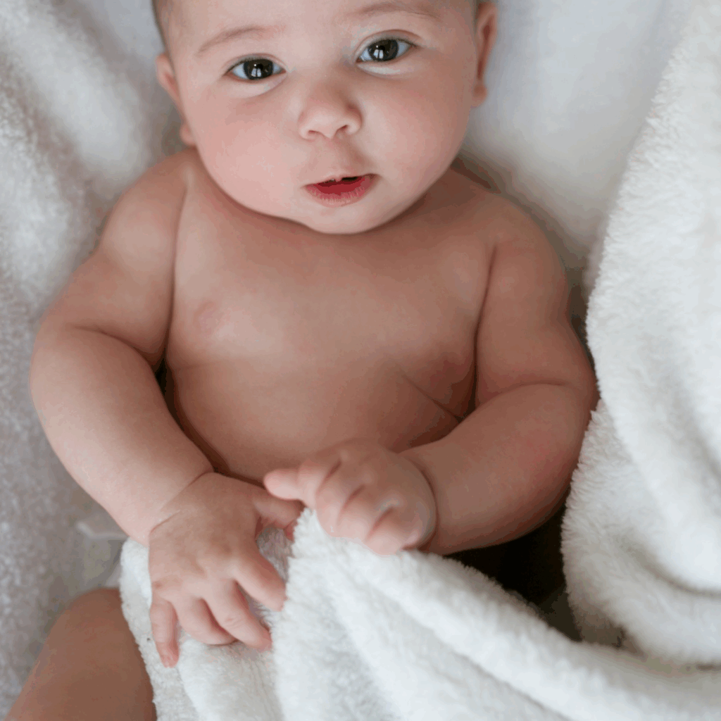 A baby lies on a towel, pulling on it to help develop their hand strength.