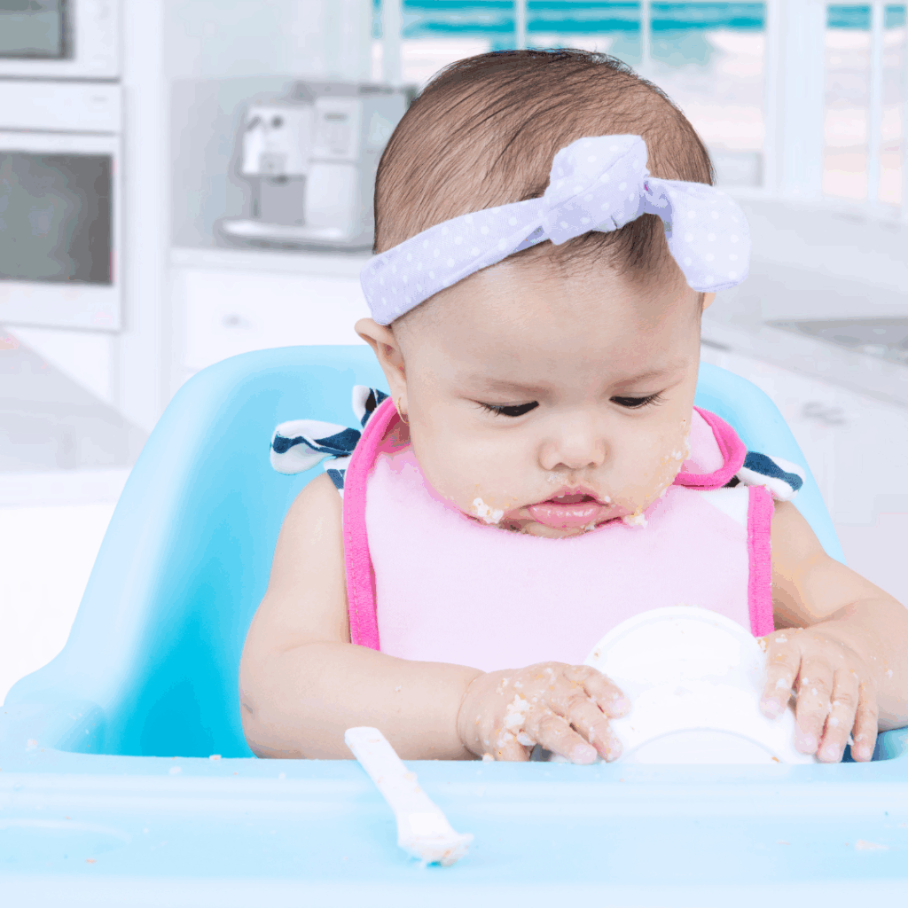 Baby eating blw food in a highchair; best first foods for babies.