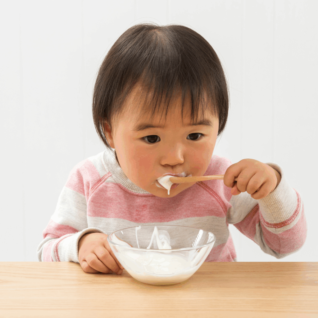 Starting solid foods by introducing top allergens as soon as possible for food allergy prevention. Baby eating solids like whole milk yogurt with a spoon, baby led weaning style.