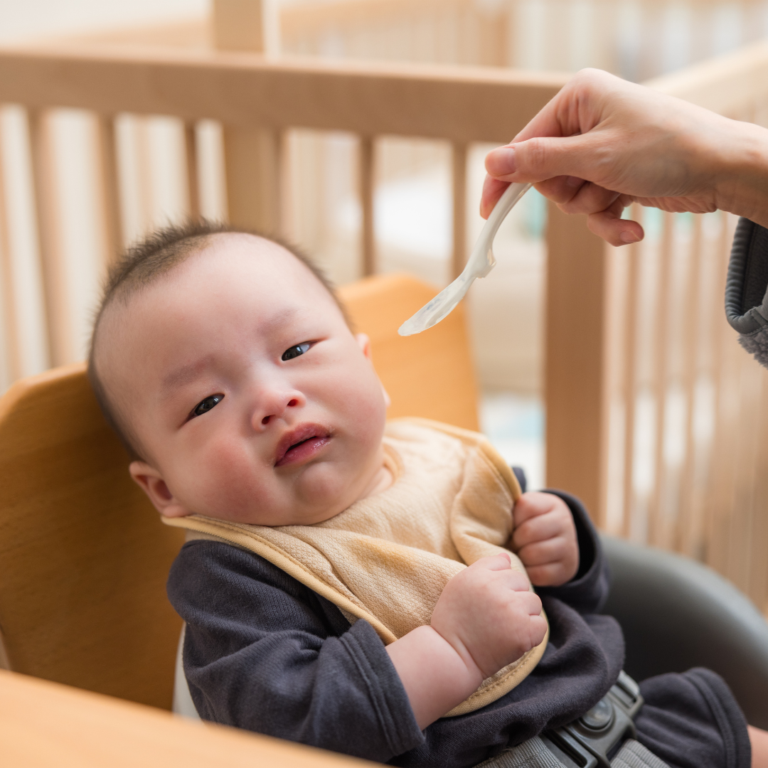 Baby turning his head away from an empty spoon offered by mom